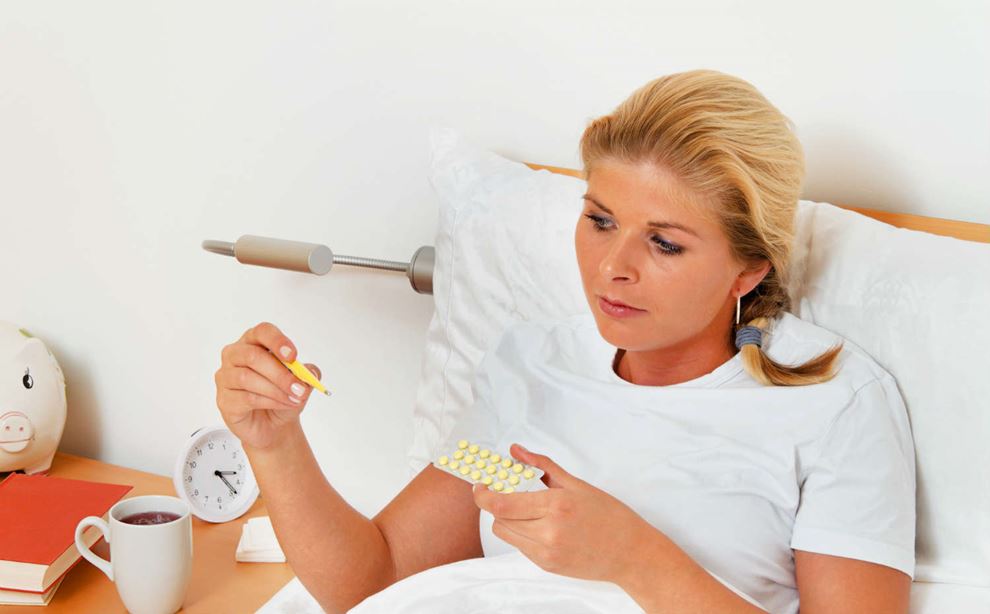 Kvinde ligger i sengen med piller og termometer