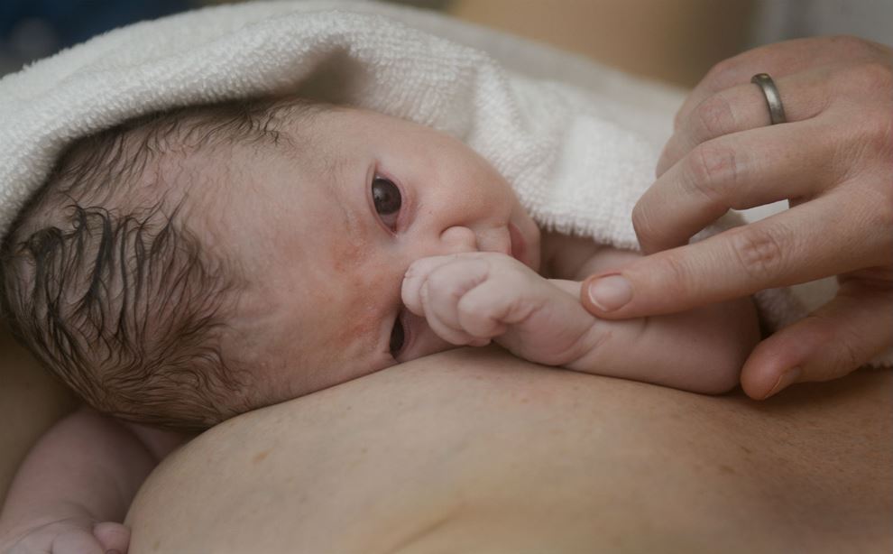 Spædbarn som ligger på maven med hånden foran ansigtet