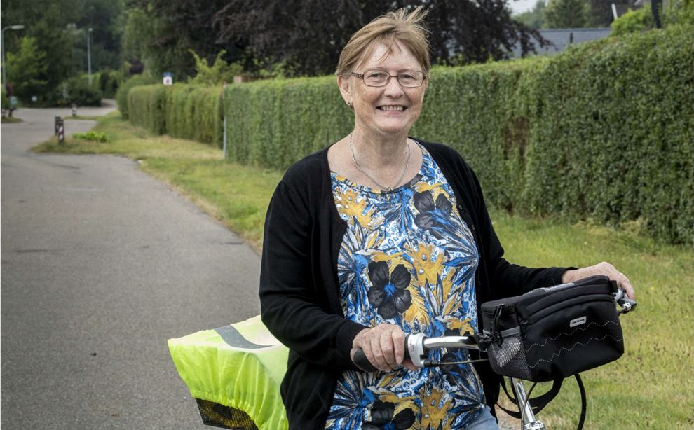 Kvinde står med sin cykel på vej med græsrabat