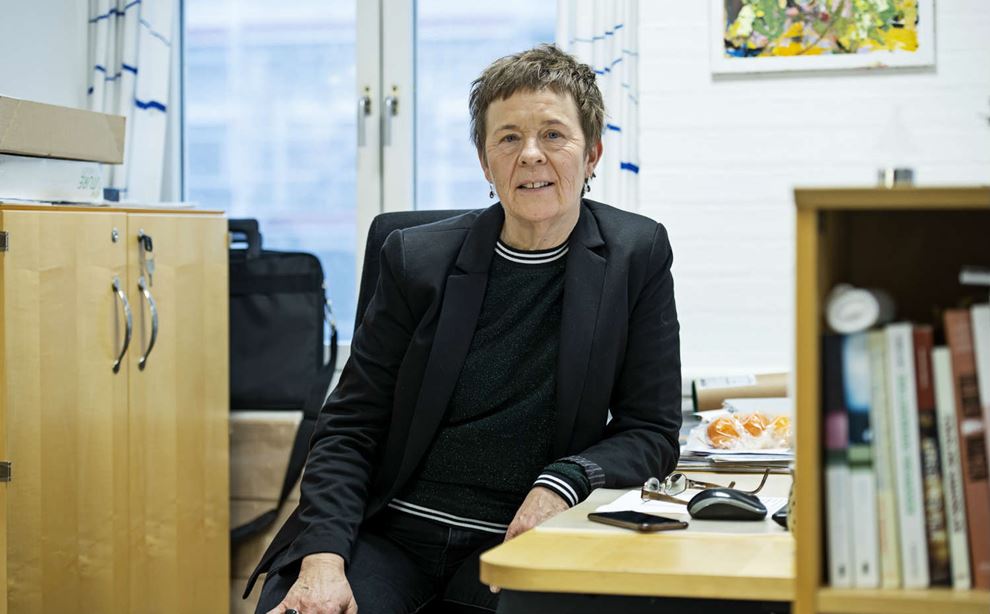 Kvinde med kort hår og sort habitjakke sidder ved et skrivebord