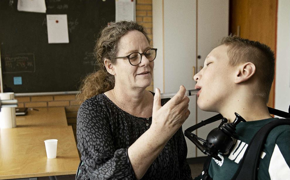 Kvinde med langt, krøllet hår giver handicappet dreng en sprøjte med medicin