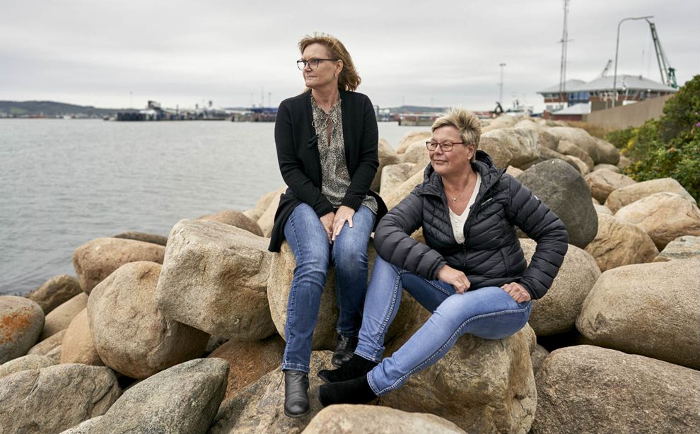To kvinder sidder på sten ved en havn