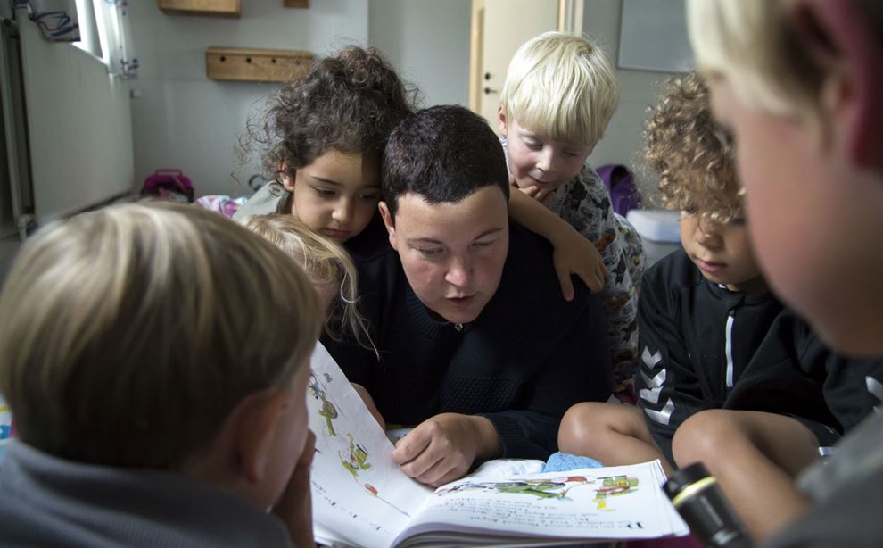 Pædagogmedhjælper læser op for en gruppe børn