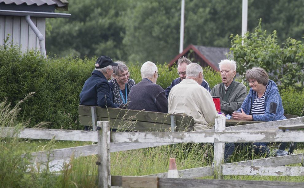 Fire mandlige demenspatienter sammen med social- og sundhedshjælper og socialpædagog spiser mad omkring et bord
