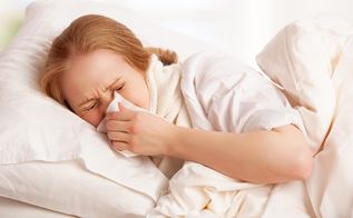 Syg kvinde ligger i seng og pudser næse