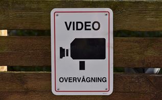 Skilt på brunt stakit oplyser om videoovervågning