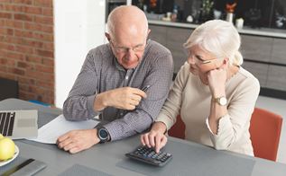 Ældre mand og kvinde sidder ved bord med regnemaskine