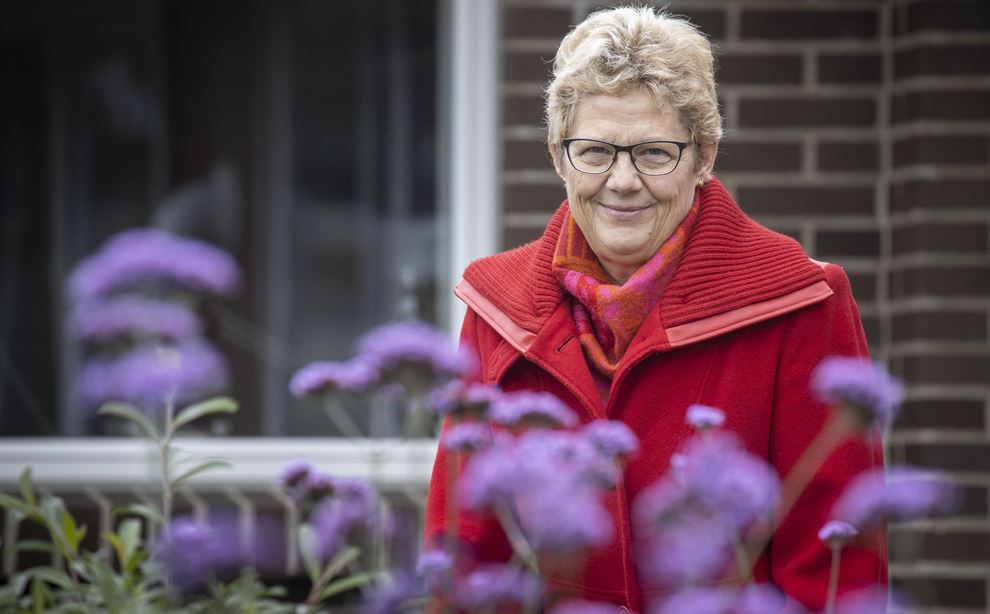 Kvinde iklædt  rød frakke i haven foran hus