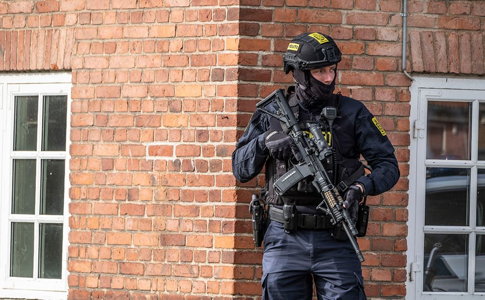Kampklædt politibetjent står op af mur med maskinegevær