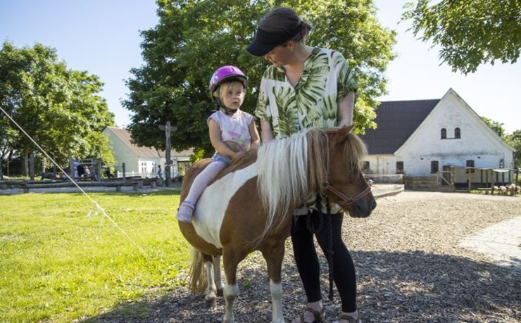 Barn rider på pony med voksen ved siden af