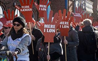 Billede af demonstration med skilte, der siger mere i løn