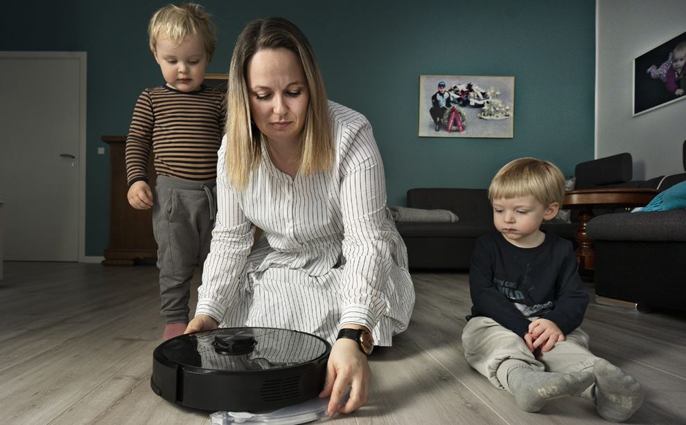 Dagplejer og to børn kigger ned på en rengøringsrobot