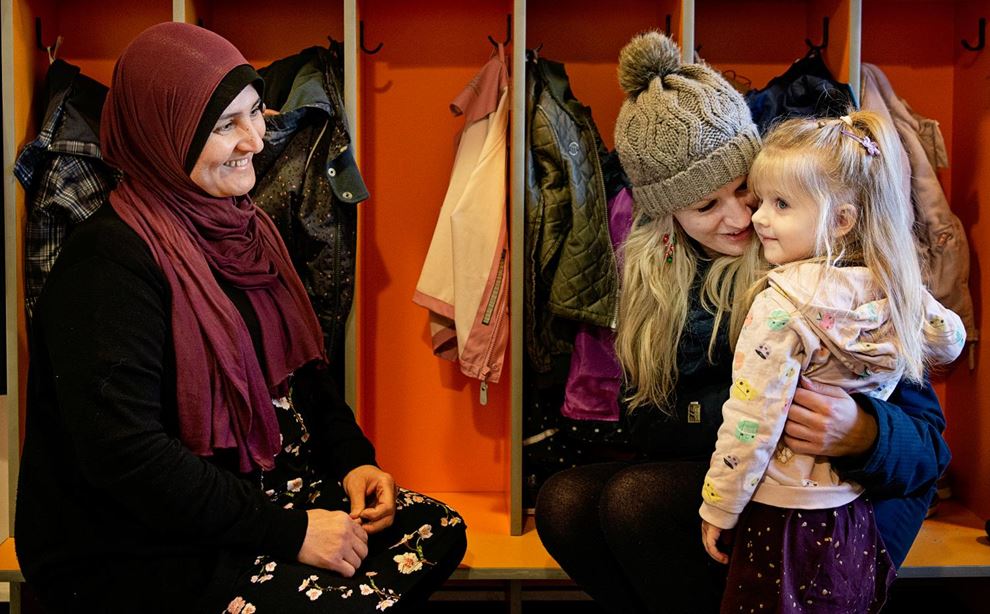 Pædagogisk assistent smiler til mor og barn i garderoben